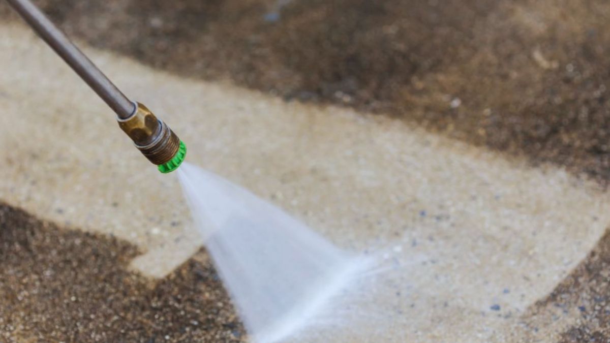 A person using a high-pressure washer to clean a concrete surface, removing dirt and grime with powerful water jets.