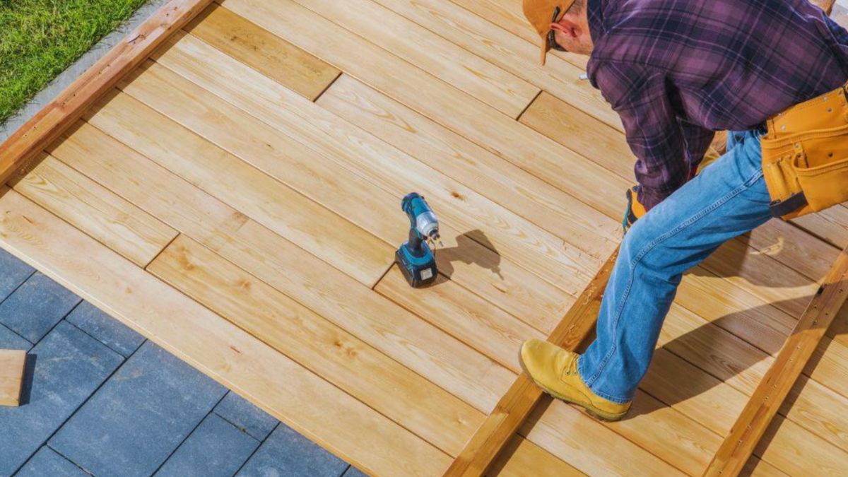 A decking contractor meticulously works on a wooden deck, showcasing craftsmanship and attention to detail.